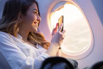 Young woman smiling and taking a photo with her phone by an airplane window