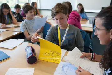 Students working in a language class with a teacher, one holding yellow study notes