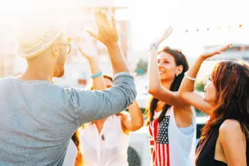 Young people high-fiving and dancing at a rooftop party at sunset with a US flag