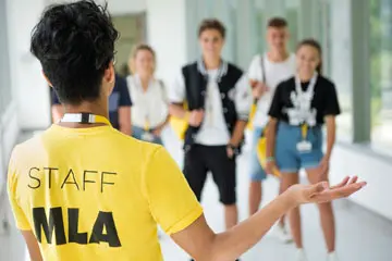 MLA staff member in yellow t-shirt welcoming a group of arriving students