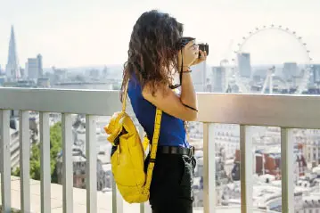 Young woman with yellow backpack photographing the London skyline and London Eye