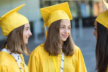 Three girls in yellow graduation gowns and caps smiling together
