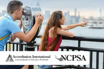 Couple looking at the New York skyline through a viewer, with accreditation logos