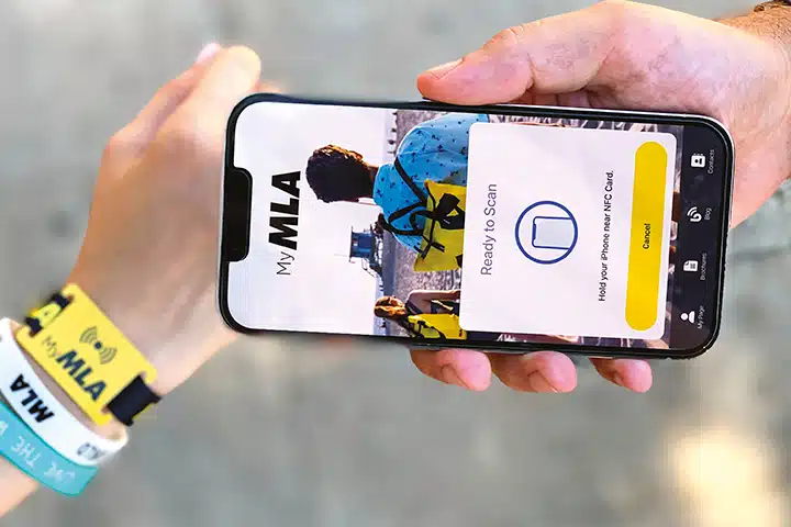Hand holding a smartphone showing the My MLA app ready to scan an NFC wristband