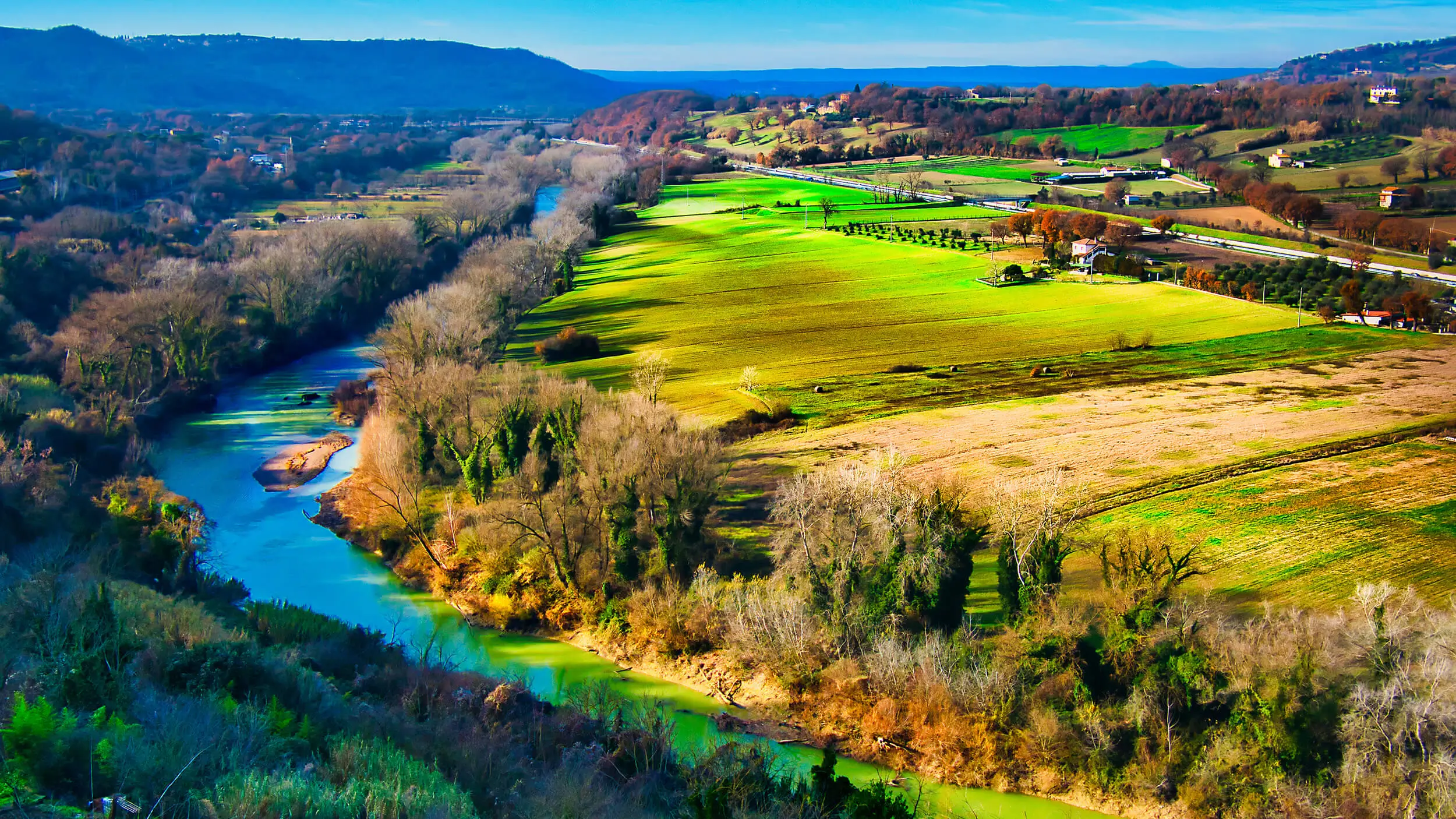 Aerial view of a green Italian river valley with fields, hills and scattered houses