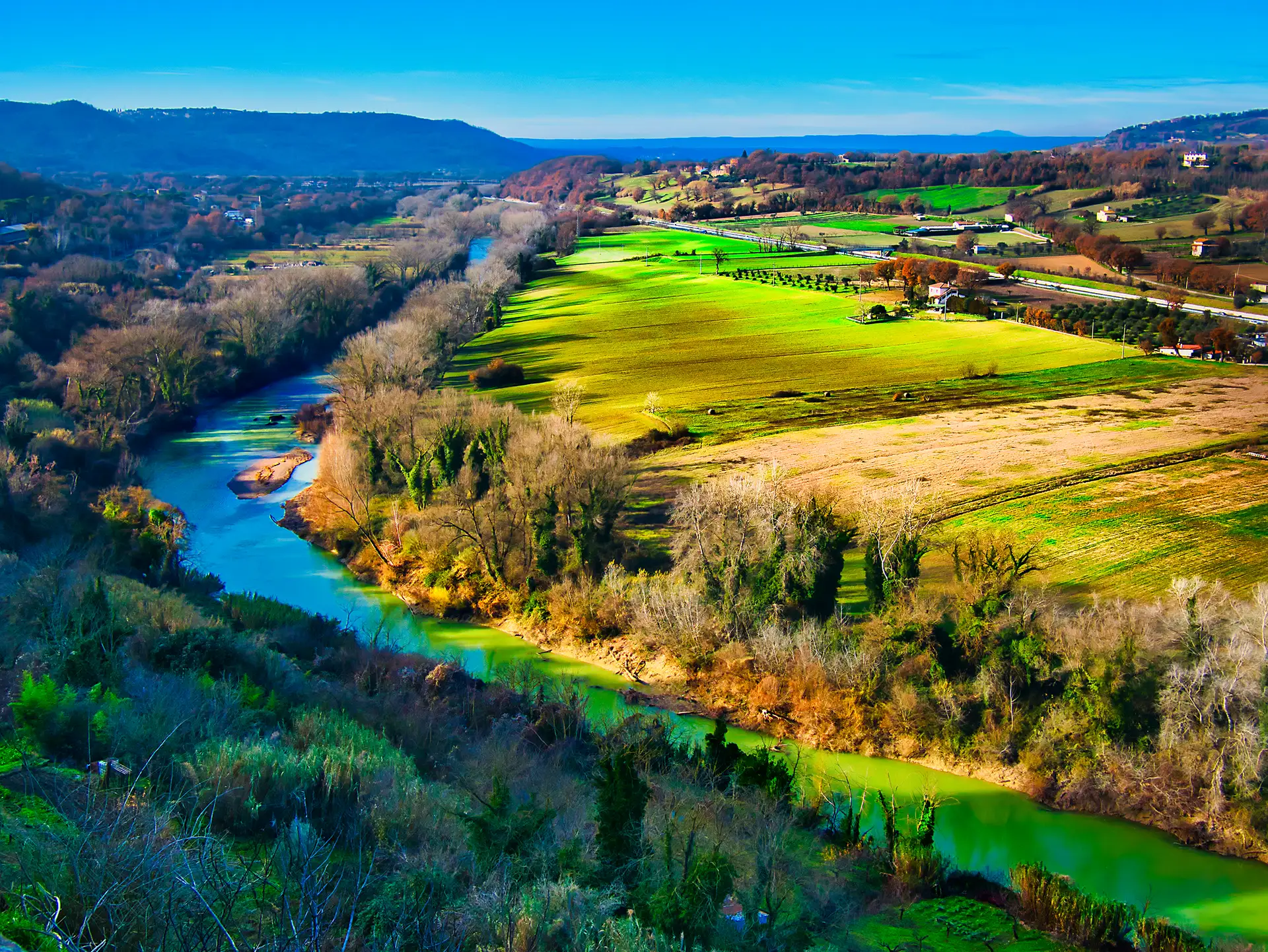Aerial view of a winding river through green fields and rolling hills in the Italian countryside