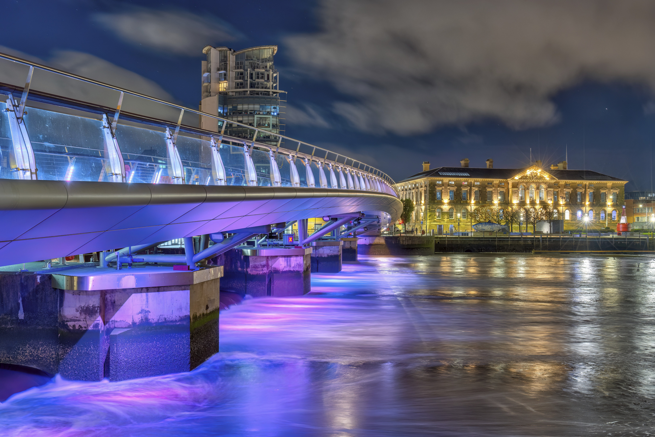 Illuminated curved footbridge over a river at night in Belfast