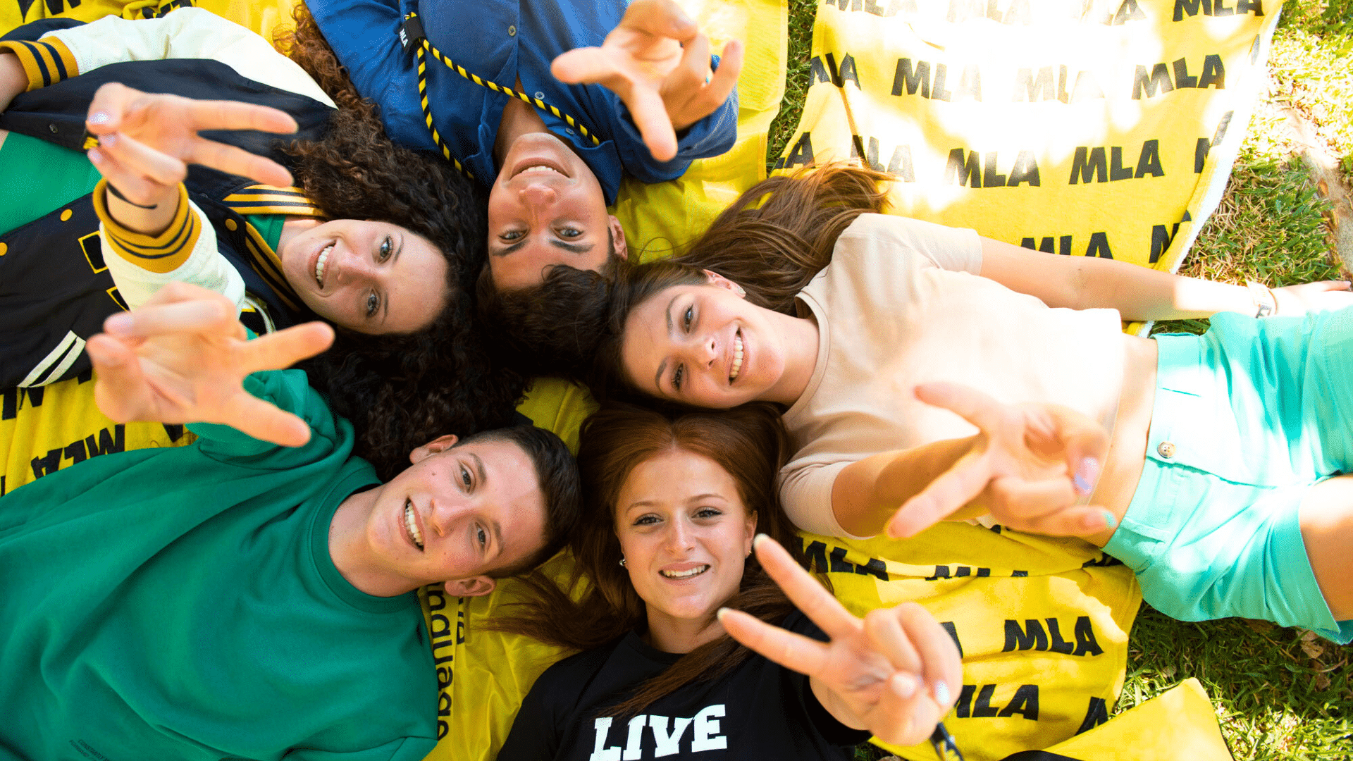 Five smiling students lying in a circle on MLA beanbags making hand signs
