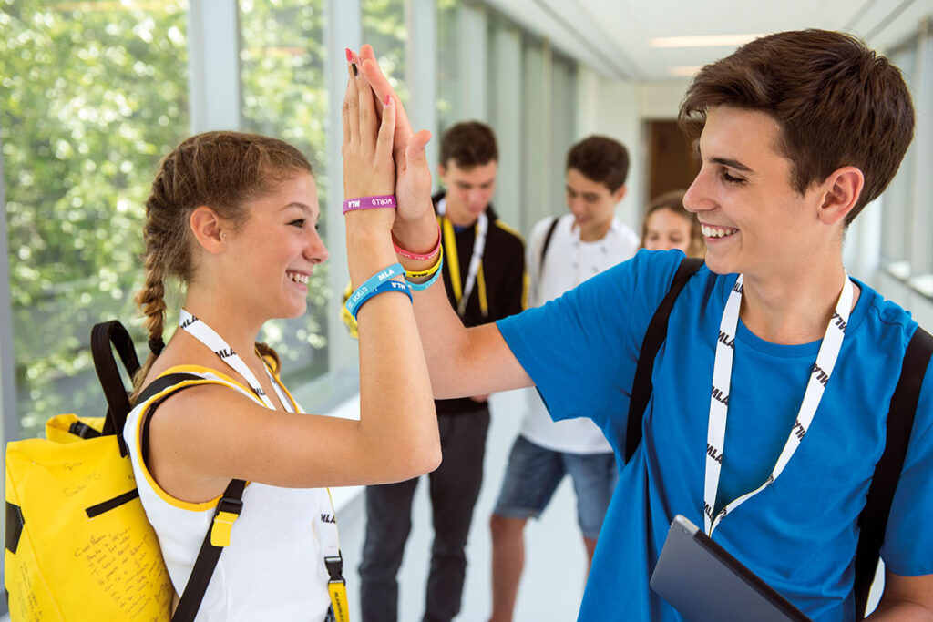 Two smiling teenage students with MLA backpacks giving each other a high five
