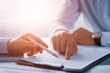 Close-up of two people reviewing and signing documents at a desk