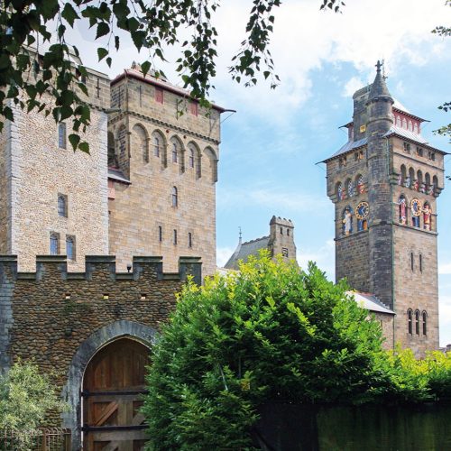 Cardiff Castle stone towers and ornate clock tower in Wales, framed by trees