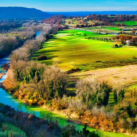 Aerial view of a green Italian river valley with fields, hills and scattered houses